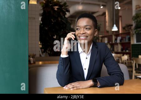 Fröhliche und fröhliche Frau, die während der Mittagspause in einem Café telefoniert, Geschäftsfrau, die fröhlich lächelt Stockfoto