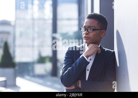 Nahaufnahme eines Büroarbeiters, müde und überfordert, hat starke Kopfschmerzen und Depressionen, einer afroamerikanischen Frau außerhalb des Büros, Stockfoto