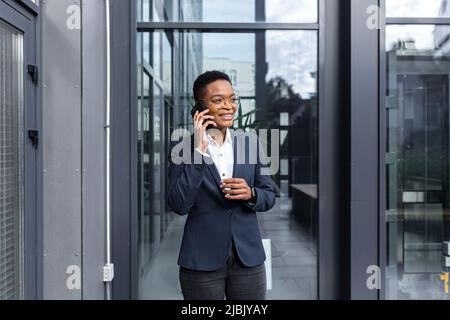 Erfolgreiche und glückliche Geschäftsfrau mit Spaß am Telefon in der Nähe des Büros, afroamerikanische Frau lächelnd reden Stockfoto