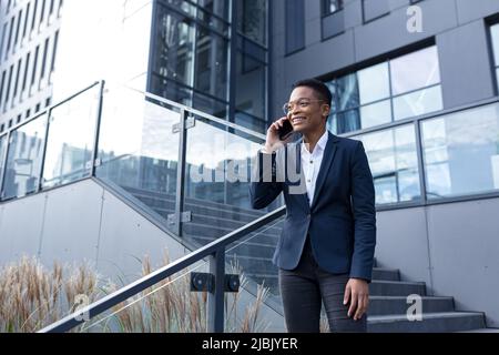 Erfolgreiche Geschäftsfrau, die außerhalb des Büros telefoniert, afroamerikanische Frau in Geschäftskleidung, kommuniziert mit Kollegen smi Stockfoto