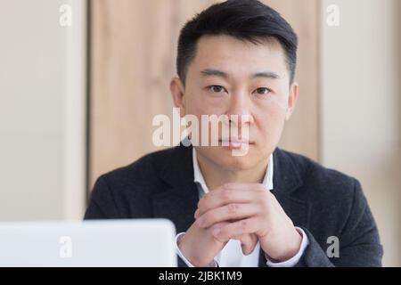 Nahaufnahme Porträt Asian nachdenklichen jungen Büroangestellter Mann am Arbeitsplatz. Stellen Sie sich einem ernsten männlichen Geschäftsführer in formellen Anzug denken über die Lösung eines Profis Stockfoto