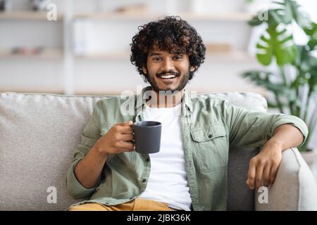 Dunkelhäutiger Mann, der Kaffee trinkt und lächelt, häusliche Einrichtung Stockfoto