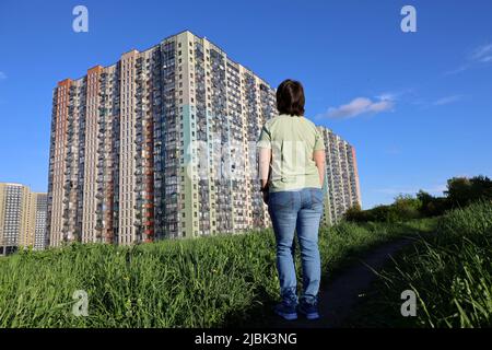 Frau auf grünem Rasen schaut auf die neuen Häuser, Wohnviertel in ökologisch sauberer Gegend. Bauindustrie und Immobilienkonzept Stockfoto