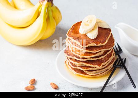 Stapel Bananenpfannkuchen mit Sirup auf einem weißen Teller, grauer Hintergrund. Veganes Rezeptkonzept. Stockfoto