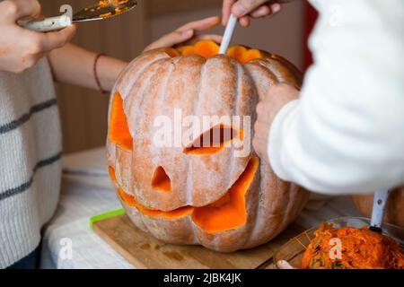 Nahaufnahme der Hand von Tochter und Vater, die Samen und faseriges Material aus einem Kürbis zieht, bevor sie zu Halloween schnitzen. Bereitet Jack-o-Laterne vor. Decora Stockfoto