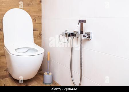 Modernes Bad. Nahaufnahme einer weißen Toilettenschüssel und einer hygienischen Dusche an der Wand Stockfoto