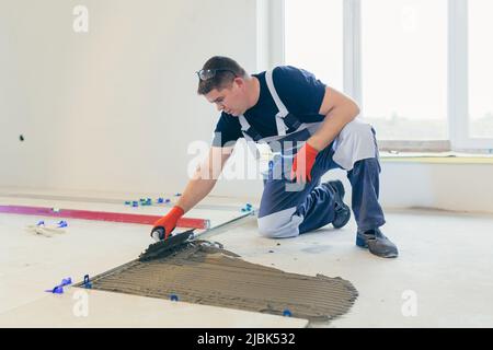 Ein männlicher Bauarbeiter installiert eine große Keramikfliese Stockfoto