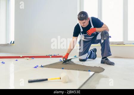 Ein männlicher Bauarbeiter installiert eine große Keramikfliese Stockfoto