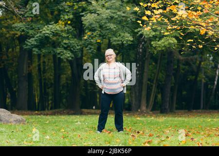 Ältere Frau, die im Park auf dem Rasen steht und Sport macht, trainiert und einen gesunden aktiven Lebensstil führt Stockfoto