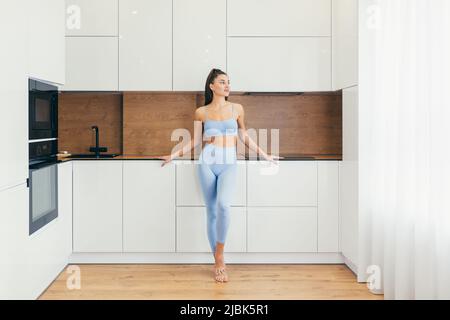 Nahaufnahme Ganzkörperportrait mit einer jungen, schönen, sportlichen Frau, Fitnesstrainer zu Hause, stehend und zur Seite schauend Stockfoto