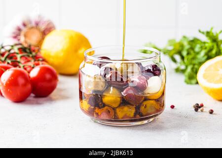 Marinierte Oliven in Glas gießen Olivenöl, weiße Küche Hintergrund. Stockfoto