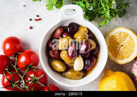 Marinierte Oliven mit Gewürz und Öl in weißer Schale, Draufsicht, grauer Hintergrund. Stockfoto