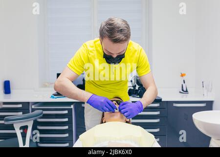 Der Zahnarzt legt eine Kappe auf den Mund einer jungen Patientin, die im Büro auf einem Zahnarztstuhl liegt. Zähne behandeln Stockfoto