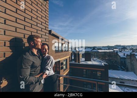 Liebende schöne junge Paar, Mann und Frau auf dem Balkon auf der Terrasse des Hauses, Sonnenlicht, küssen umarmt Stockfoto