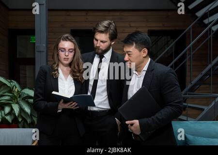 Ein Team von drei Mitarbeitern, die einen Geschäftsplan und eine Strategie besprechen, einen Laptop betrachten und sich in einem Besprechungsraum befinden Stockfoto