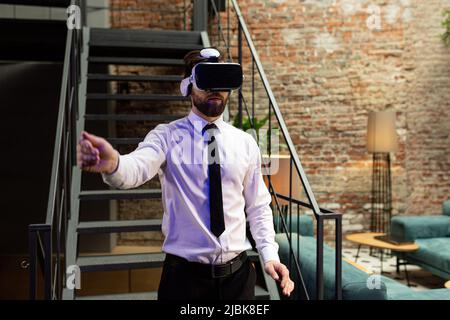 Ein Mann Büroleiter in formeller Kleidung trägt Virtual Reality vr Brille Swiping scrollende Online-Bilder in modernen Büro. Augmented Reality-Konzept Stockfoto