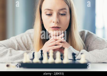 Nahaufnahme eines Bildportraits von einer jungen schönen Frau, die zu Hause Schach spielt, studiert, denkt, konkurrierend, in Quarantäne Stockfoto