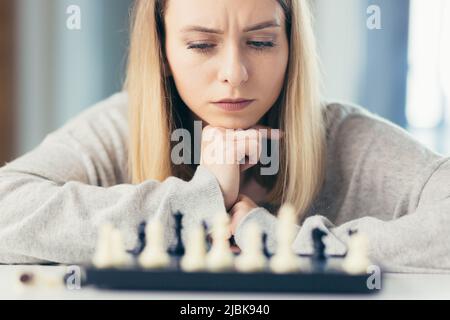 Nahaufnahme eines Bildportraits von einer jungen schönen Frau, die zu Hause Schach spielt, studiert, denkt, konkurrierend, in Quarantäne Stockfoto