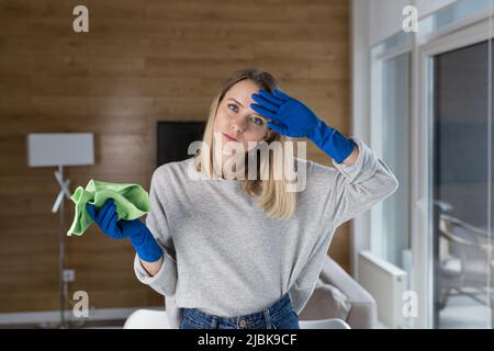 Müde junge Frau putzt, Hausfrau, wäscht Tisch mit Lappen in Gummihandschuhen zu Hause, im Büro, im Hotel Stockfoto