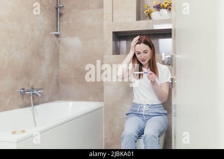 Glückliche kaukasische junge Frau freut sich über positiven Schwangerschafts-Kit-Test auf Mutterschaft. Nahaufnahme Porträt der Frau zu Hause Überprüfung Ergebnis und Emotionen e Stockfoto