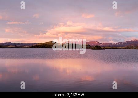 Landschaft mit Bergen, Hügeln und Kratern unter einem spektakulären Himmel spiegelt sich im See Myvatn, Island Stockfoto