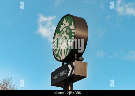 Eine Fahrt durch Startbucks Schild, hoch stehend mit dem Hintergrund eines blauen Himmels mit wispy Wolken, eine Person, eine Tasse und eine Nachbarschaft auf einmal Stockfoto