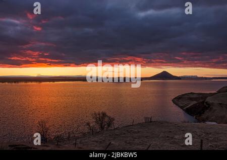 Die Sonne scheint durch eine kleine Lücke in den Wolken am nordwestlichen Horizont und bringt den See Myvatn und die Wolken darüber in ein spektakuläres Licht Stockfoto