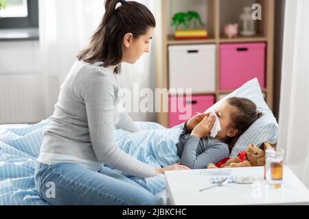 Mutter und kranke kleine Tochter blasen Nase im Bett Stockfoto