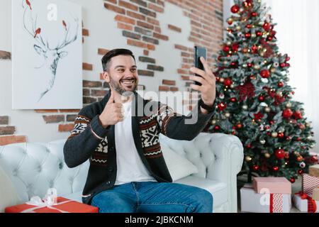 Der Mann selbst feiert Weihnachten zu Hause, erhält Grüße von Freunden kommuniziert per Video über die Anwendung auf dem Telefon Stockfoto