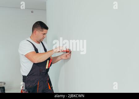 Männlicher Arbeiter professionelle Elektriker installiert Steckdose in der Wohnung nach der Reparatur Stockfoto