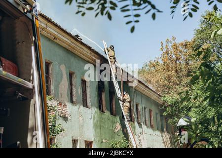 Russland, Rostow am Don - 2. Juni 2022: Feuerwehrleute stehen auf der Treppe und löschen einen Brand auf dem Dach eines verlassenen Hauses mit einem Hydranten. Stockfoto