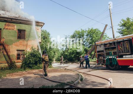 Russland, Rostov-on-Don - 2. Juni 2022: Feuerwehrmann löscht einen Brand in einem verlassenen Haus mit einem Hydranten, in der Nähe schieben Rettungskräfte eine Leiter Stockfoto