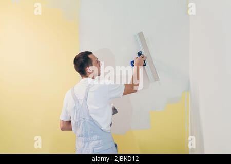 Ein Arbeiter trägt mit einem Spachtel Kitt an die Wände der Wohnung auf, repariert in einem neuen Haus Stockfoto