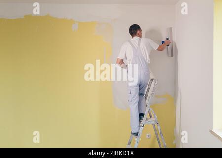 Ein Arbeiter trägt mit einem Spachtel Kitt an die Wände der Wohnung auf, repariert in einem neuen Haus Stockfoto