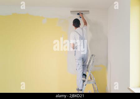 Ein Arbeiter trägt mit einem Spachtel Kitt an die Wände der Wohnung auf, repariert in einem neuen Haus Stockfoto
