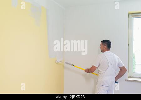 Arbeiter Mann trägt Farbe und Kitt auf die Wände in der Wohnung, macht Reparaturen in einem neuen Haus Stockfoto