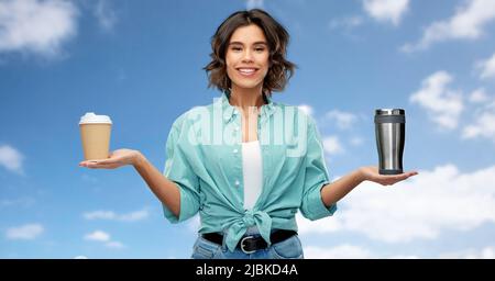 Frau, die Thermobecher und Papierkaffeebecher vergleicht Stockfoto