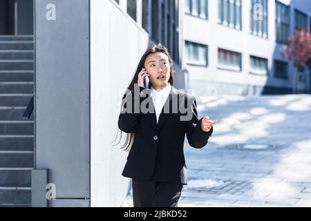 Schöne asiatische Frau am Telefon zu sprechen, Geschäftsfrau auf einer Pause zu Fuß in der Nähe des Büros Stockfoto