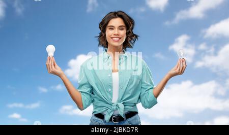 Lächelnde Frau, die verschiedene Glühbirnen vergleicht Stockfoto