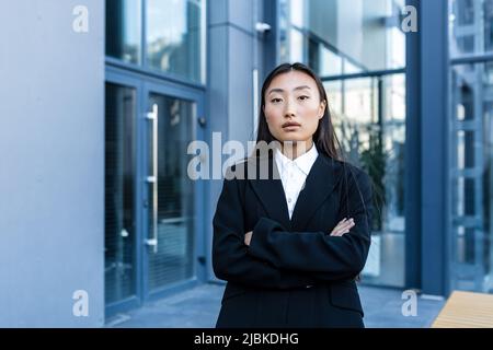 Erfolgreiche Geschäftsfrau nachdenklich und ernst mit gekreuzten Armen, außerhalb des Büros, asiatische Frau, die Kamera anschaut Stockfoto