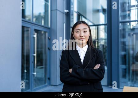 Erfolgreiche Geschäftsfrau nachdenklich und ernst mit gekreuzten Armen, außerhalb des Büros, asiatische Frau, die Kamera anschaut Stockfoto