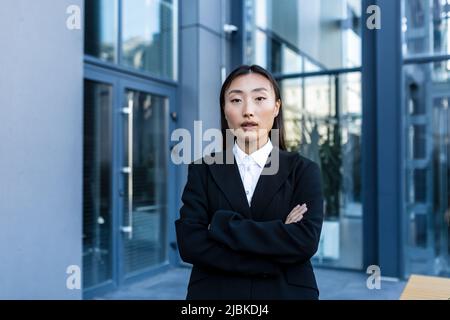 Erfolgreiche Geschäftsfrau nachdenklich und ernst mit gekreuzten Armen, außerhalb des Büros, asiatische Frau, die Kamera anschaut Stockfoto