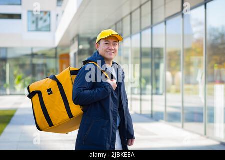Wanderkurier Lieferung Mann Asian lächelnd und Blick auf die Kamera, hat einen großen gelben Rucksack für die Lieferung von Lebensmitteln Stockfoto