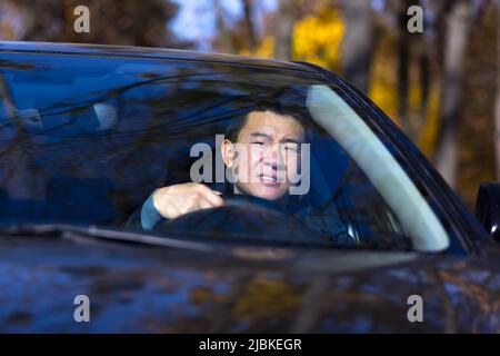 Ein nachdenklicher Asiat sitzt im Auto, der Fahrer wartet und ist traurig Stockfoto