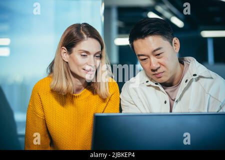 Nahaufnahme, ein Team von 2 Büromitarbeitern, ein asiatischer Mann und eine Frau, die einen Computermonitor betrachten Stockfoto