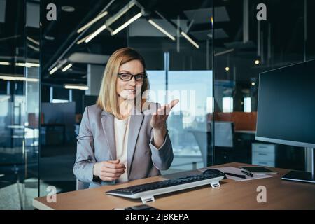 Videoanruf einer glücklichen und erfolgreichen Geschäftsfrau, eine Mitarbeiterin hat ein Online-Meeting, berät Mitarbeiter, schaut auf die Webcam und erklärt fröhlich Stockfoto