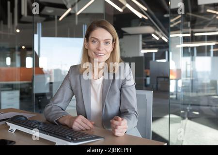 Porträt einer schönen Geschäftsfrau, die die Kamera anschaut und lächelt, Videoanruf mit Kollegen, einer Geschäftsfrau, die im modernen Büro am Computer arbeitet Stockfoto