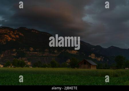 Dämmerung nach dem Sonnenuntergang in Dornbirn, Vorarlberg, Österreich. Tolle Stimmung mit interessanteren graublau Wolken, grünen Wiesen und Haus Stockfoto