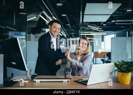 Ein Team von Mitarbeitern, ein Mann und eine Frau Geschäftsleute, arbeiten im Büro, freuen sich über den Erfolg, klatschen zusammen Stockfoto