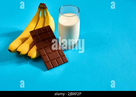 Glas Milch mit Bananen und Schokolade auf blauem Hintergrund Stockfoto